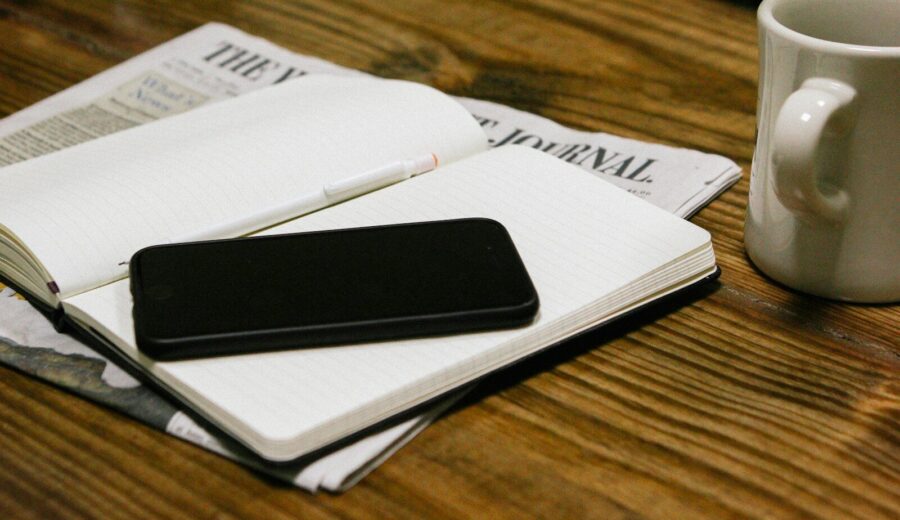 Periódico abierto, taza y teléfono móvil sobre una mesa de madera